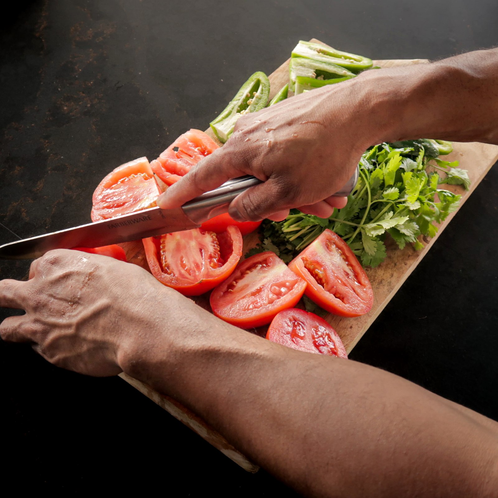 Hands chopping tomatoes, cilantro and jalapeño on a wooden board